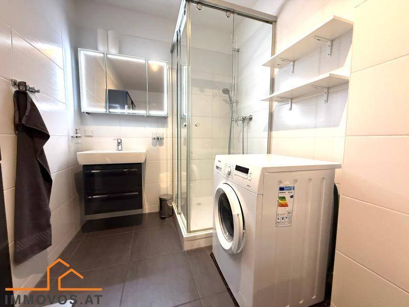 Helles Badezimmer mit Glasdusche, modernem Waschbecken und integrierter Waschmaschine.