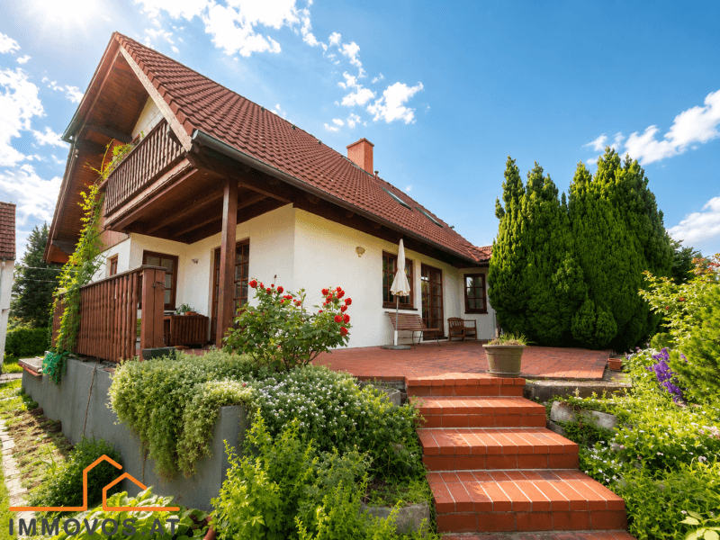 Charmantes Einfamilienhaus mit großer Terrasse, Garten und Balkon unter blauem Himmel.