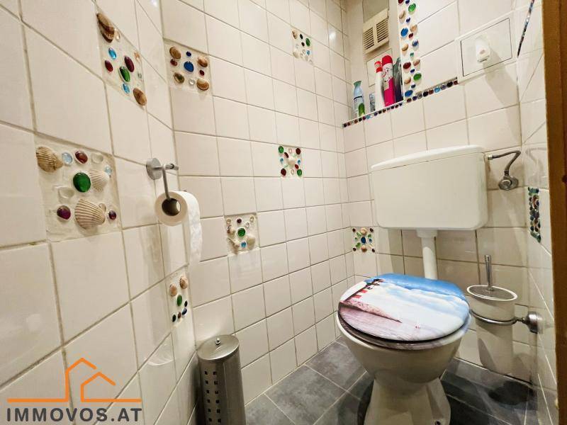 Kleines WC mit weißen Fliesen und dekorativen Muschel- und Glaselementen.