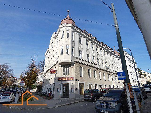 Historisches Eckgebäude mit markanter Architektur und Geschäften im Erdgeschoss an einer belebten Straße.