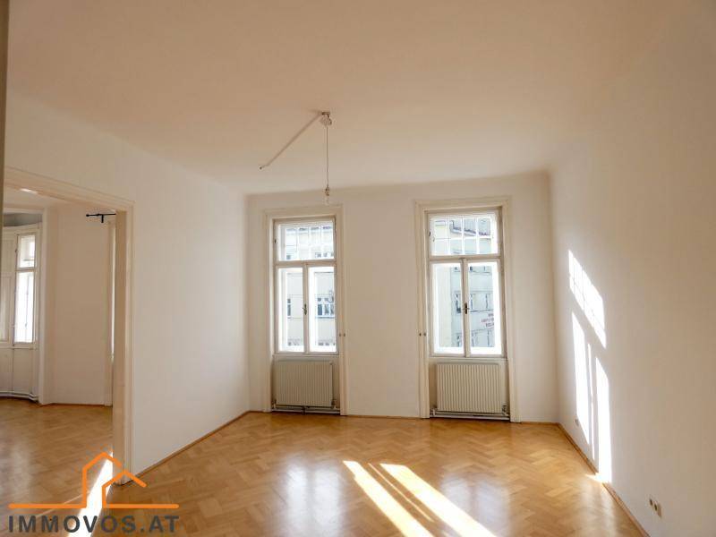 Helles Zimmer mit Fischgrätparkett, weißen Wänden und viel natürlichem Licht durch zwei Fenster.