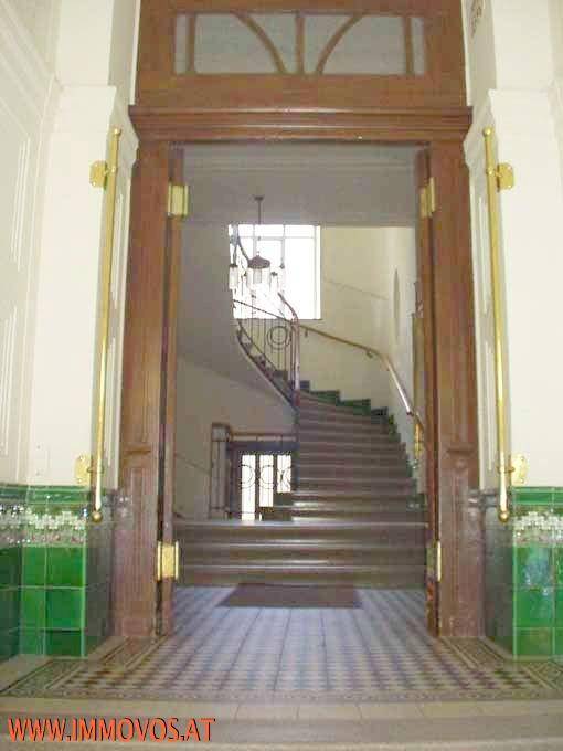 Repräsentativer Eingangsbereich mit breiter Holztreppe, grünen Fliesen und hohen Decken.