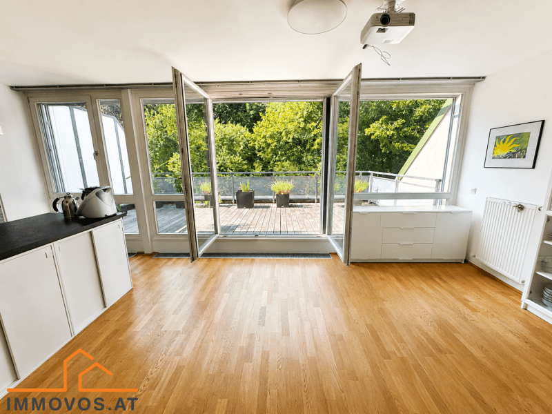 Heller Wohnbereich mit Holzboden und großen Fenstern, die zur Dachterrasse führen.