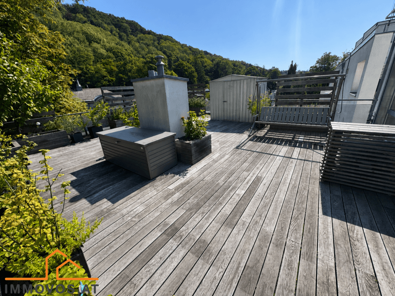 Große Dachterrasse mit Holzboden, Schaukel und Stauraum, umgeben von grünen Hügeln.