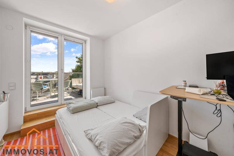 Schlafzimmer mit Balkonzugang, Holzboden und modernem Schreibtisch.