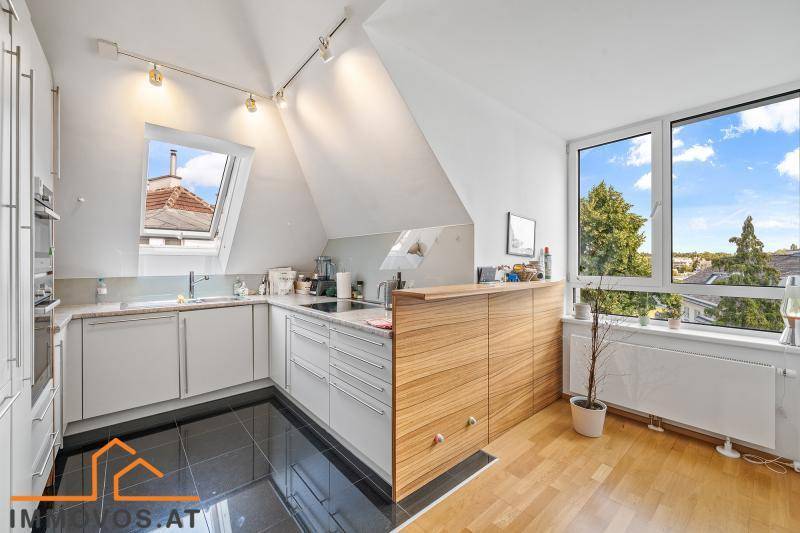 Moderne Küche mit Dachschrägen, weißen Schränken, Holzelementen und Blick ins Grüne.