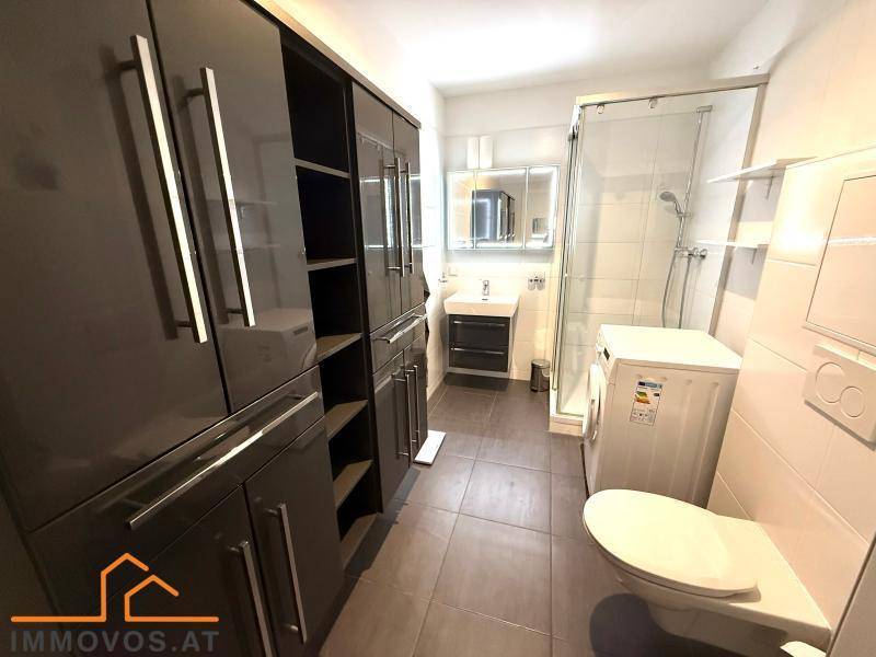 Modernes Badezimmer mit Dusche, Waschmaschine und viel Stauraum in dunklen Schränken.