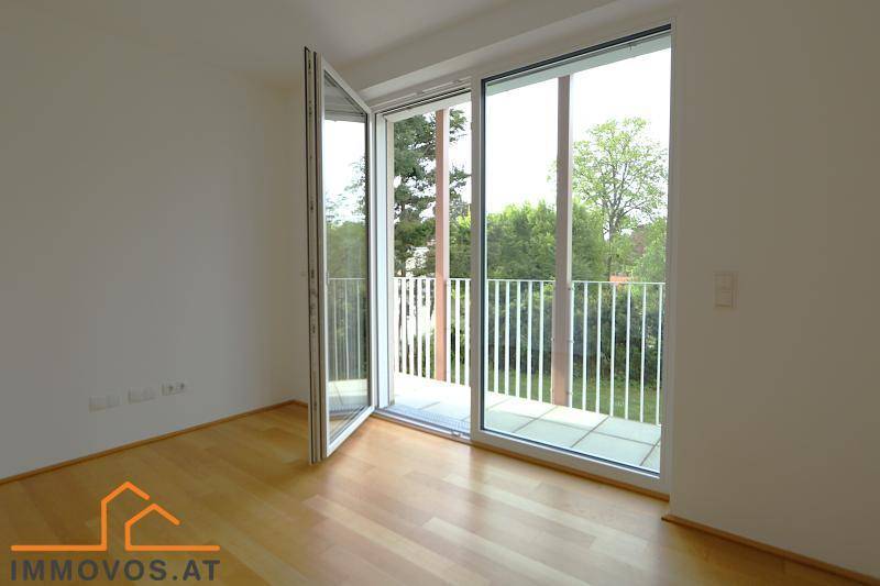 Helles Zimmer mit Parkettboden und Zugang zu einem Balkon mit Blick ins Grüne.