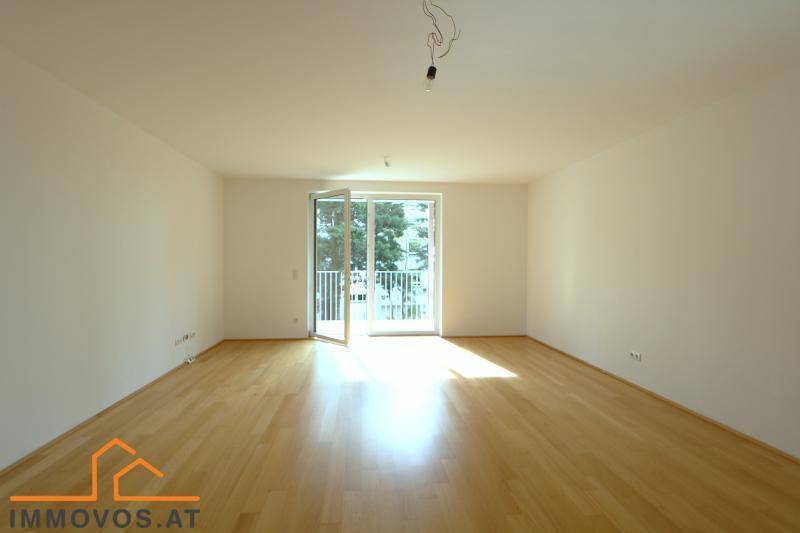 Lichtdurchfluteter Wohnbereich mit hellem Parkettboden und großen Fenstern zum Balkon.