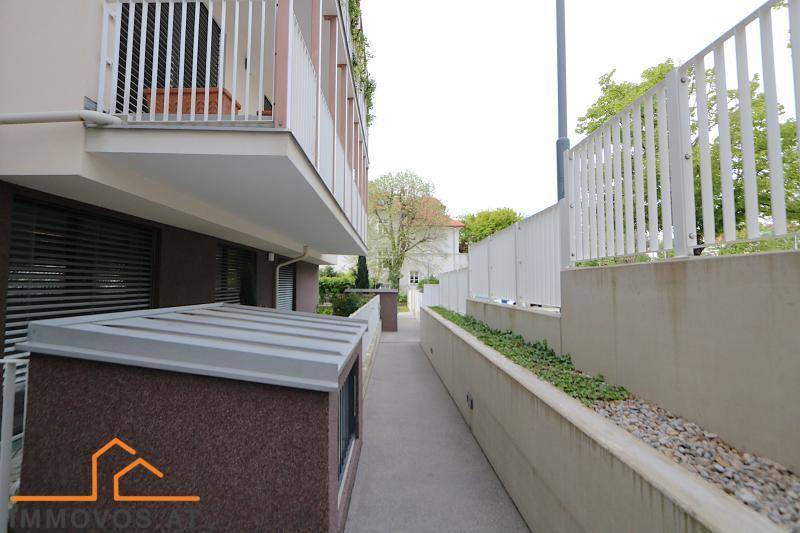 Seitlicher Zugang zum Gebäude mit einer Rampe und einem kleinen Gartenbereich.