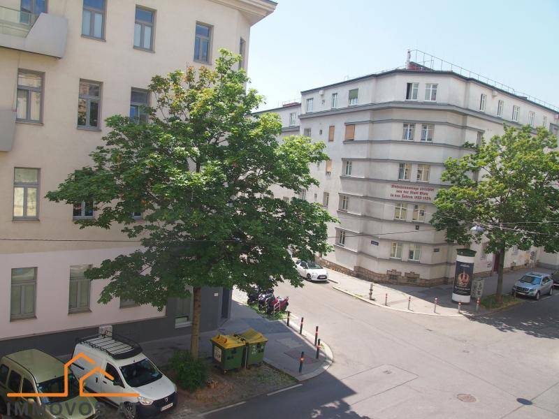 Blick von oben auf eine Straßenecke mit parkenden Autos, Bäumen und umliegenden Wohngebäuden.