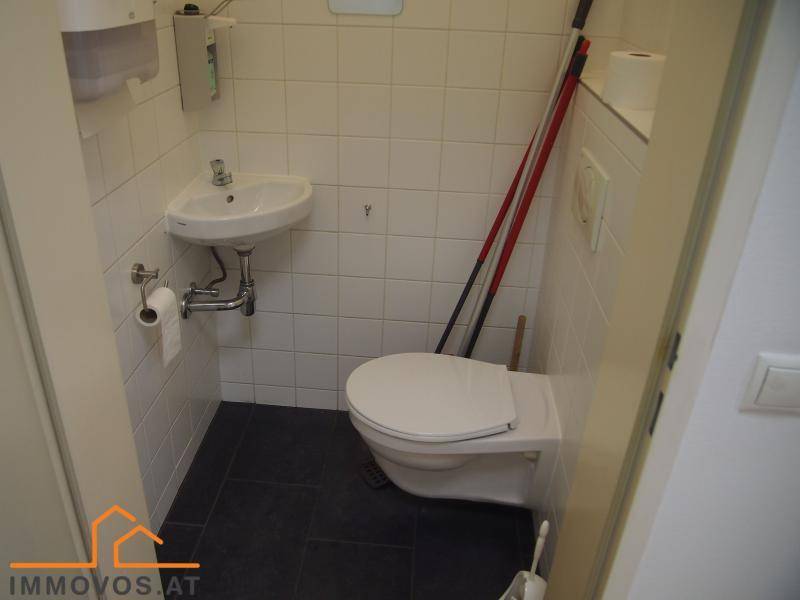 Kleines WC mit weißen Wandfliesen, dunklem Boden, Waschbecken und wandhängender Toilette.