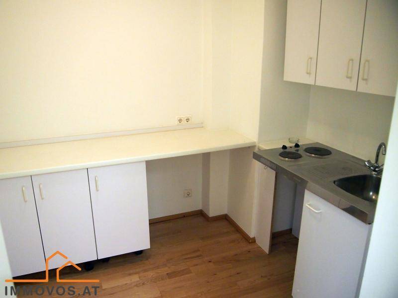Kleine Küchenzeile mit weißen Schränken, Spüle und Kochplatten, ideal für eine Singlewohnung oder Büro.
