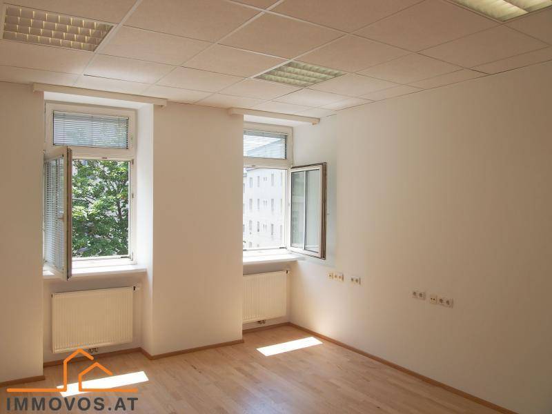 Geräumiges, leeres Zimmer mit zwei Fenstern, Holzfußboden und Deckenbeleuchtung, ideal für Büronutzung.