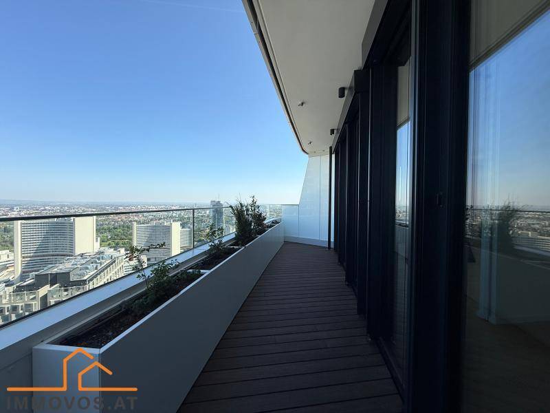 Langer Balkon mit Glasbrüstung, Pflanzen und weitem Stadtblick von einem Hochhaus.