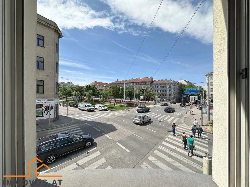 Blick aus dem Fenster auf eine belebte Straßenkreuzung mit Stadtverkehr und Fußgängern.