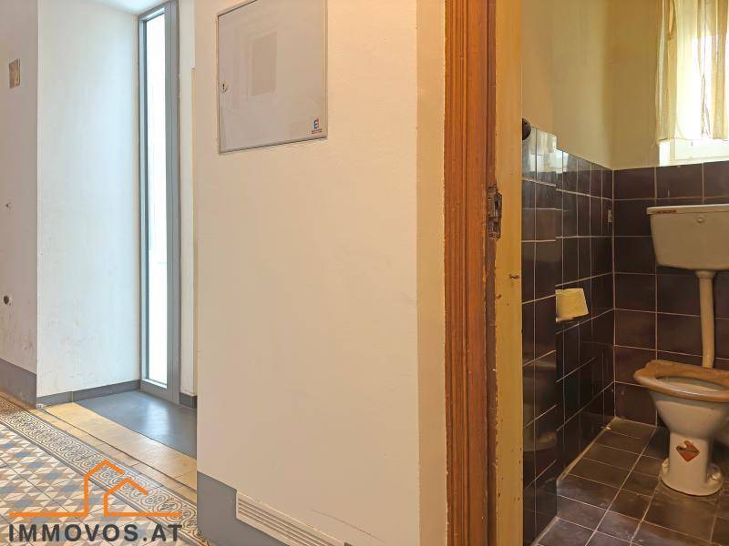 Separate Toilette mit dunklen Fliesen und Fenster, funktional und einfach ausgestattet.
