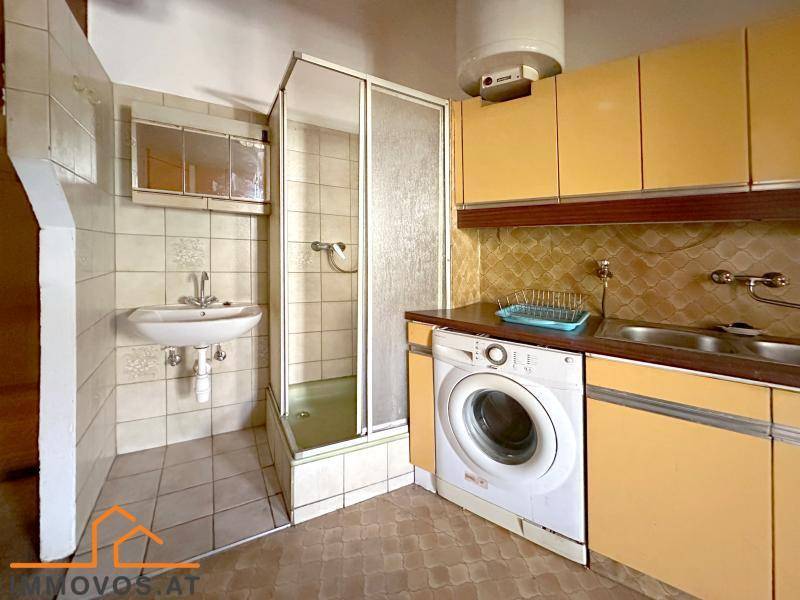 Kleines Badezimmer mit Dusche und Waschbecken, integriert in den Küchenbereich, funktional gestaltet.