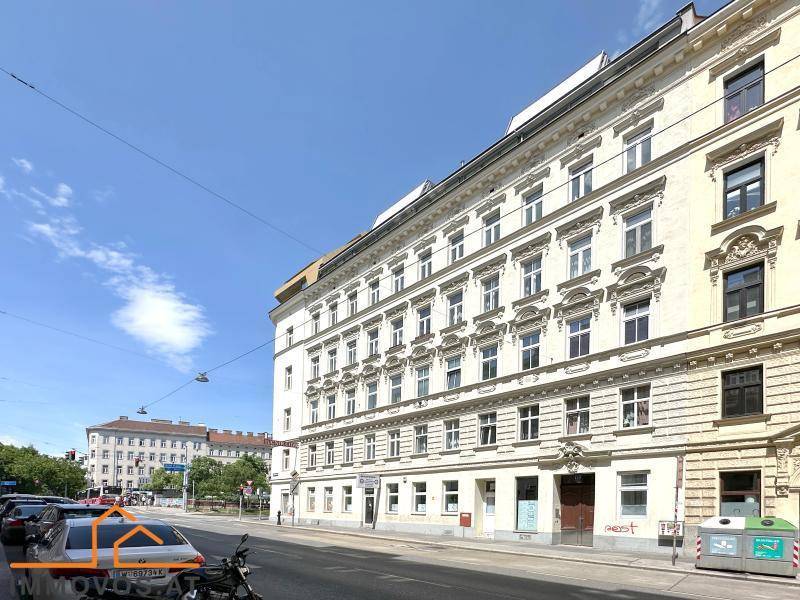 Lange Fassade eines Altbaugebäudes entlang einer Straße mit parkenden Autos.