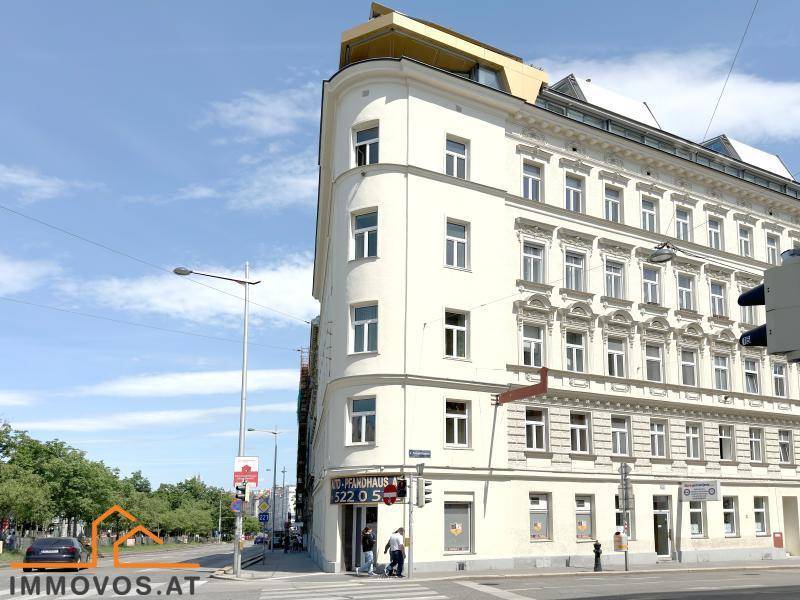 Eckgebäude mit klassischer Architektur an einer belebten Straße unter strahlend blauem Himmel.