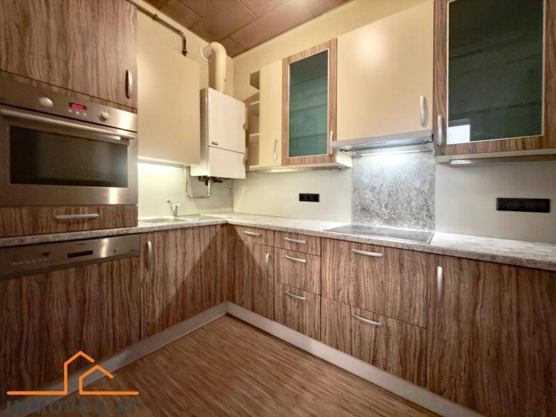 Funktionale Küche mit Holzschränken, Einbaugeräten wie Backofen und Geschirrspüler sowie einem Boiler.