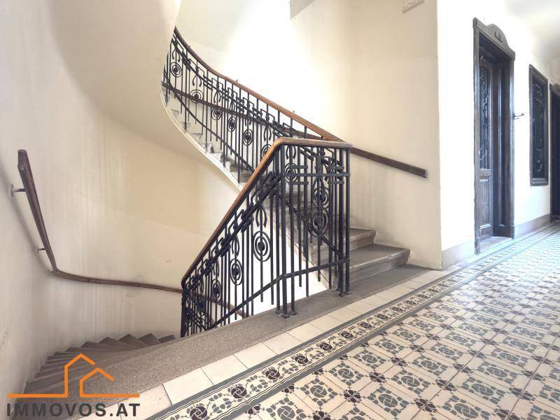 Elegantes Treppenhaus mit schmiedeeisernem Geländer und gemustertem Fliesenboden in einem Altbau.
