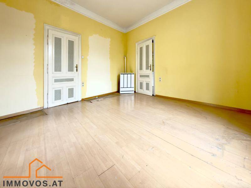 Leeres Zimmer mit gelben Wänden, zwei Türen und einem Ofen, bereit für neue Einrichtungsideen.