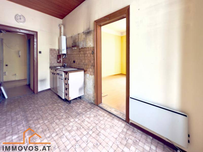 Blick in die Küche mit Fliesenboden, Heizkörper und Zugang zu einem weiteren Zimmer.