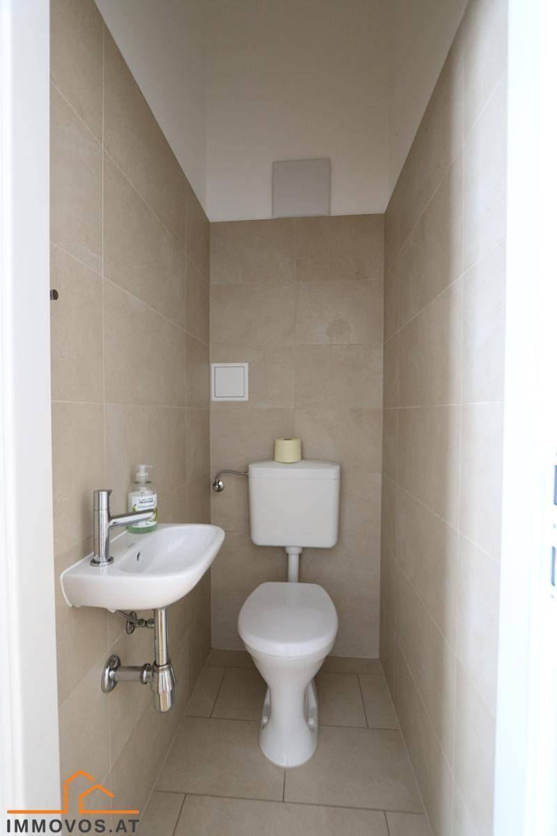 Separates WC mit kleiner Handwaschbecken und beigefarbenen Fliesen, funktional und praktisch.
