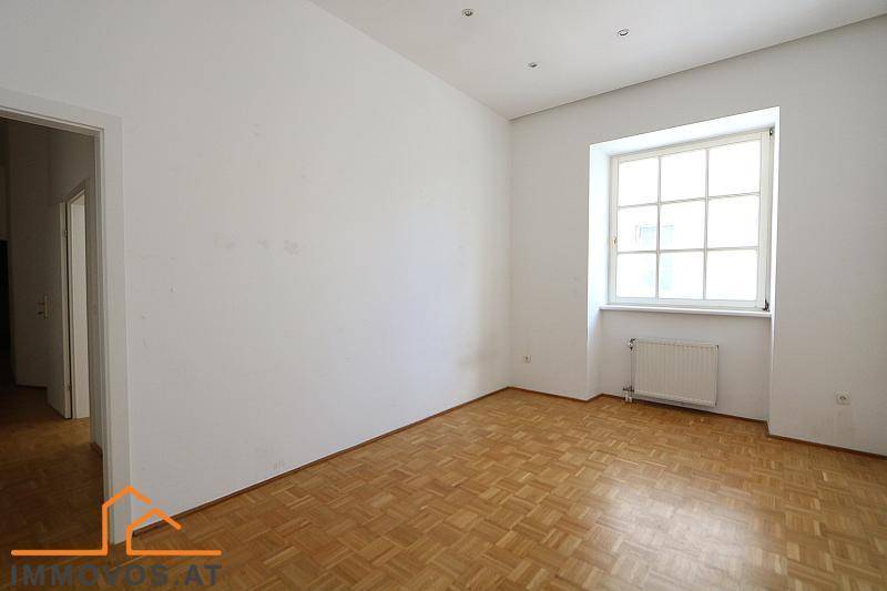 Unmöblierter Raum mit Parkettboden und einem großen Fenster, das viel Licht spendet.