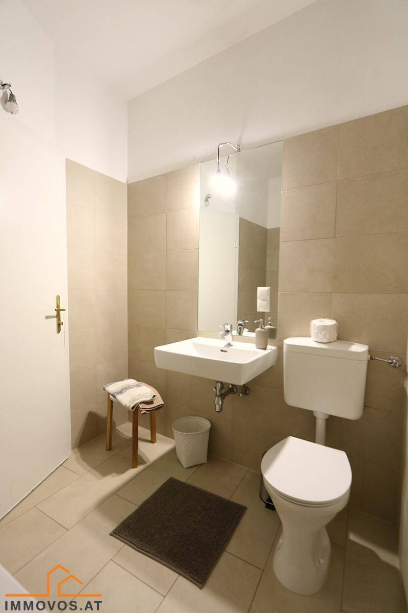 Modernes Badezimmer mit beigefarbenen Fliesen, Waschbecken und Toilette, hell und sauber.