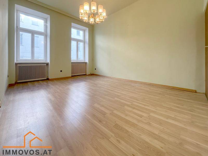 Helles Zimmer mit Laminatboden, zwei großen Fenstern und einem eleganten Kronleuchter.