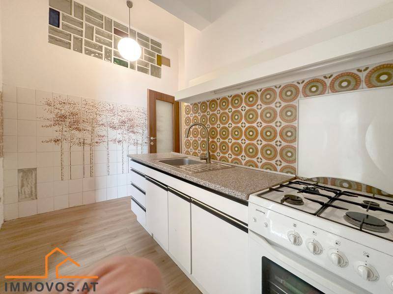 Funktionale Küche mit Gasherd, weißen Schränken und auffälligen Retro-Fliesen an der Wand.