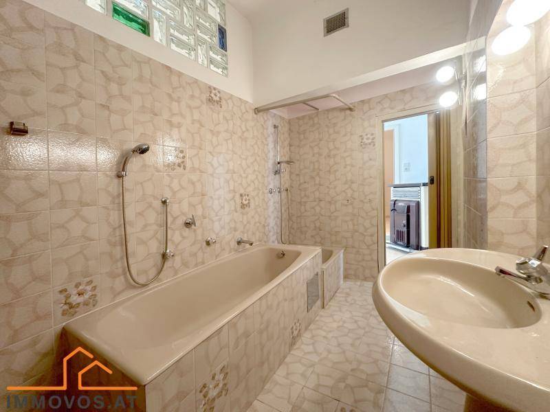 Badezimmer mit beigefarbenen Fliesen, Badewanne und Waschbecken, im Stil der 80er Jahre.