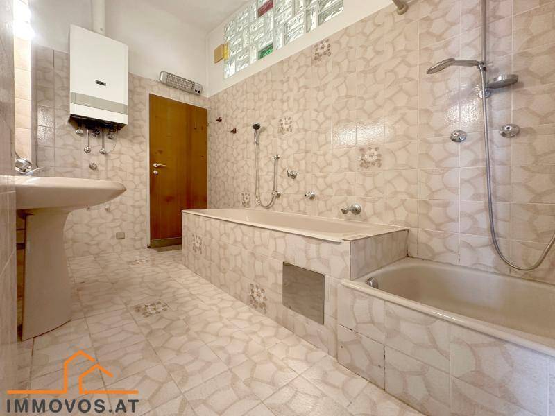 Badezimmer mit beigefarbenen Fliesen, Badewanne und Waschbecken, im Stil der 80er Jahre.