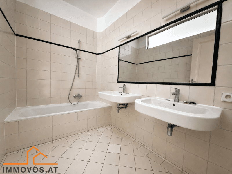 Funktionales Badezimmer mit Badewanne, Doppelwaschbecken und hellen Fliesen.