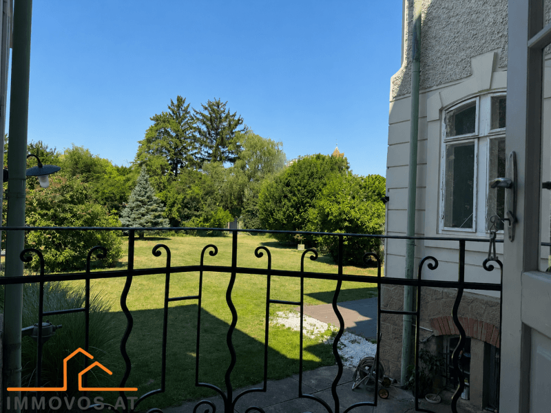Blick von einem Balkon mit schmiedeeisernem Geländer auf den weitläufigen grünen Garten.