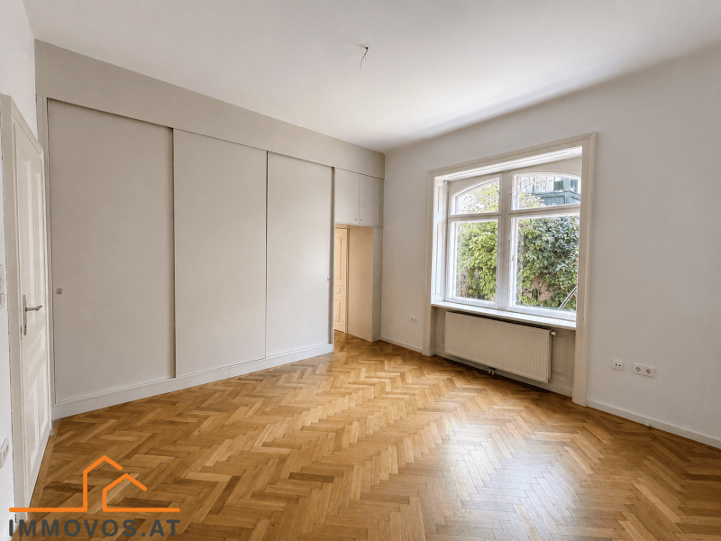 Geräumiges Schlafzimmer mit integrierten Kleiderschränken, Fischgrätparkett und Blick ins Grüne.