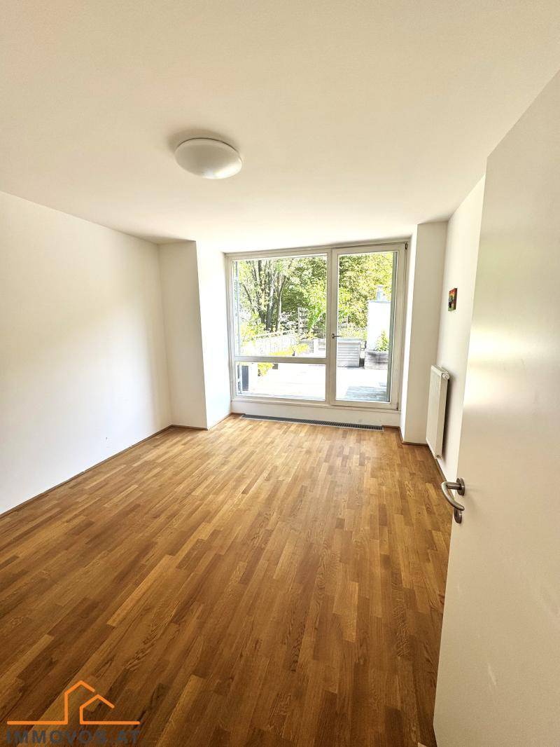 Helles Zimmer mit Holzboden und großen Fenstern, die viel Tageslicht hereinlassen und zur Terrasse führen.