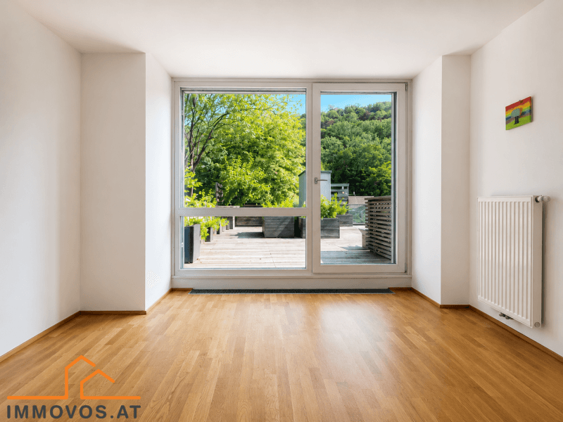 Großes Fenster in einem hellen Raum mit Blick auf die Terrasse und die grüne Umgebung.