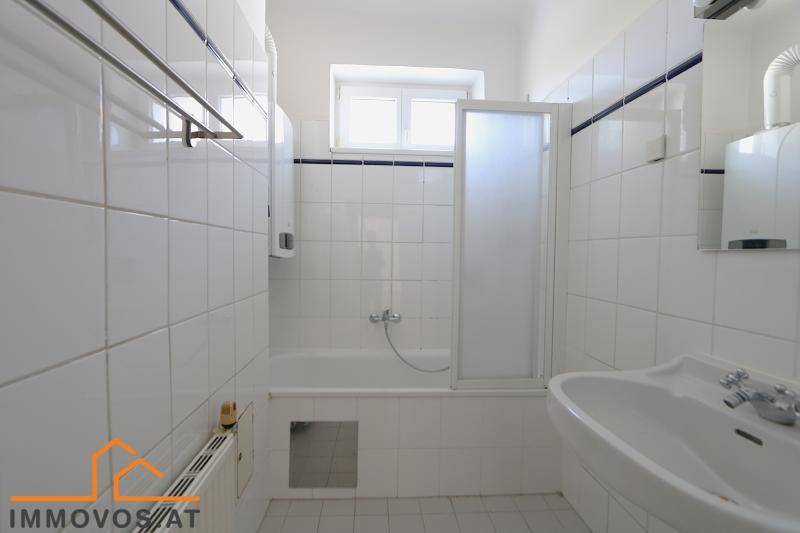 Gefliestes Badezimmer mit Badewanne, Duschabtrennung und Fenster.