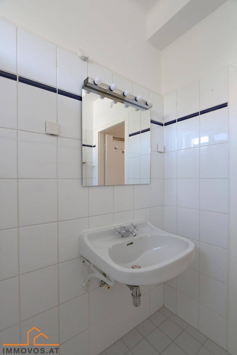 Badezimmer mit weißem Waschbecken, Spiegel und Fliesen an den Wänden.