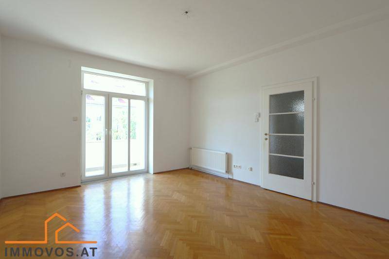 Geräumiges Wohnzimmer mit Fischgrätparkett und Zugang zu einem hellen Balkon.
