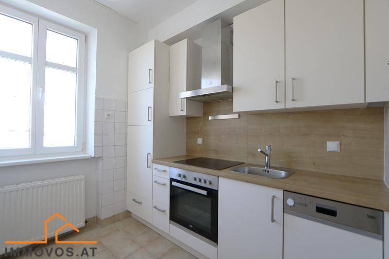 Moderne Einbauküche mit weißen Schränken, Holzoptik-Arbeitsplatte und Fenster.
