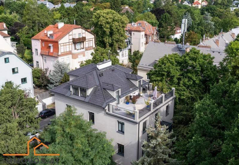 Luftaufnahme eines modernen Wohngebäudes mit Dachterrasse, umgeben von üppiger grüner Landschaft.