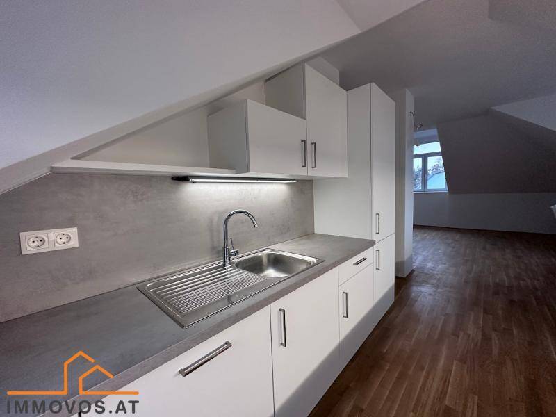 Kleine Küchenzeile im Dachgeschoss mit weißen Schränken, Spüle und grauer Arbeitsplatte auf Holzparkettboden.