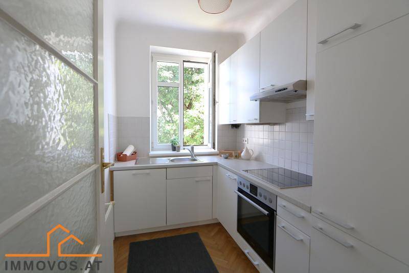 Moderne weiße Küche mit Einbaugeräten, Fenster und Blick ins Grüne.