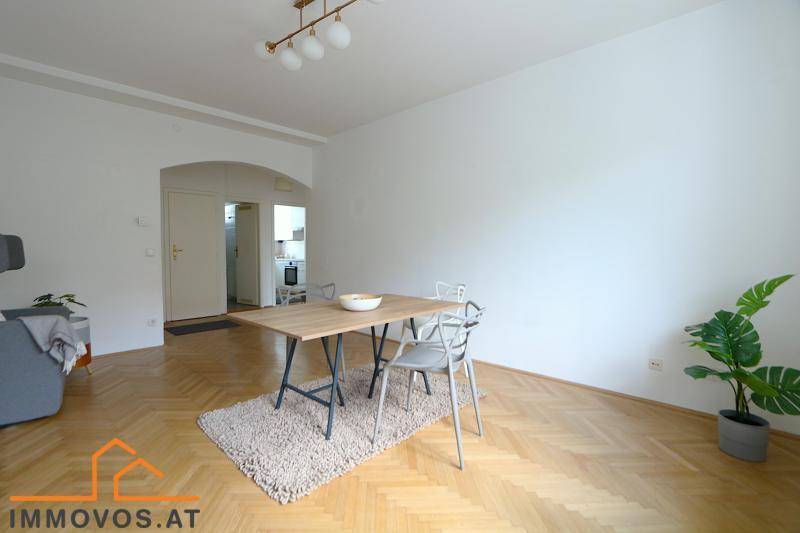 Geräumiger Wohn-Essbereich mit hellem Fischgrätparkett und Zugang zur Küche.