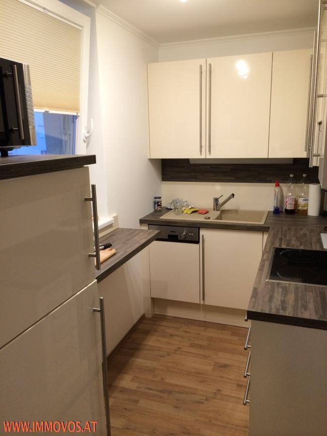 Moderne Einbauküche mit hellen Hochglanzfronten, dunkler Arbeitsplatte und Laminatboden.