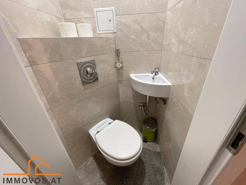 Modern gefliestes Gäste-WC mit wandhängender Toilette und kleinem Eckwaschbecken.